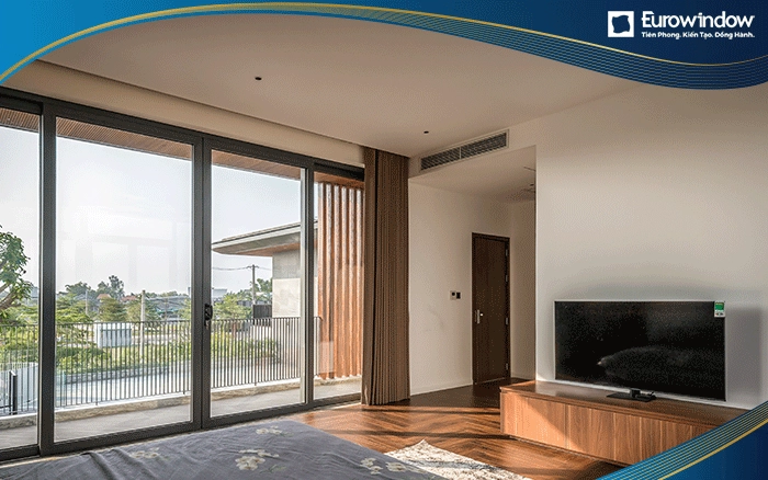 Eurowindow sử dụng cửa đi mở quay với kích thước cánh lớn kết hợp với vách kính cố định 2 bên màu xám để thay thế một mảng tường lớn trong phòng ngủ, giúp lấy nắng tối ưu, đem lại không gian nghỉ ngơi thoáng đãng