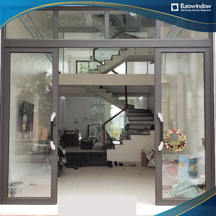 Cửa đi nhôm xoay trượt 4 cánh màu nâu xám lắp đặt ở phòng khách tạo điểm nhấn ấn tượng cho căn phòng
