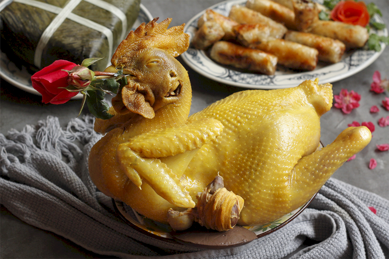 Gà trống luộc vàng ươm, mỏ ngậm hoa hồng đỏ với thế ngẩng cao đầu giúp đánh thức vượng khí cho mảnh đất. (Nguồn: Internet)